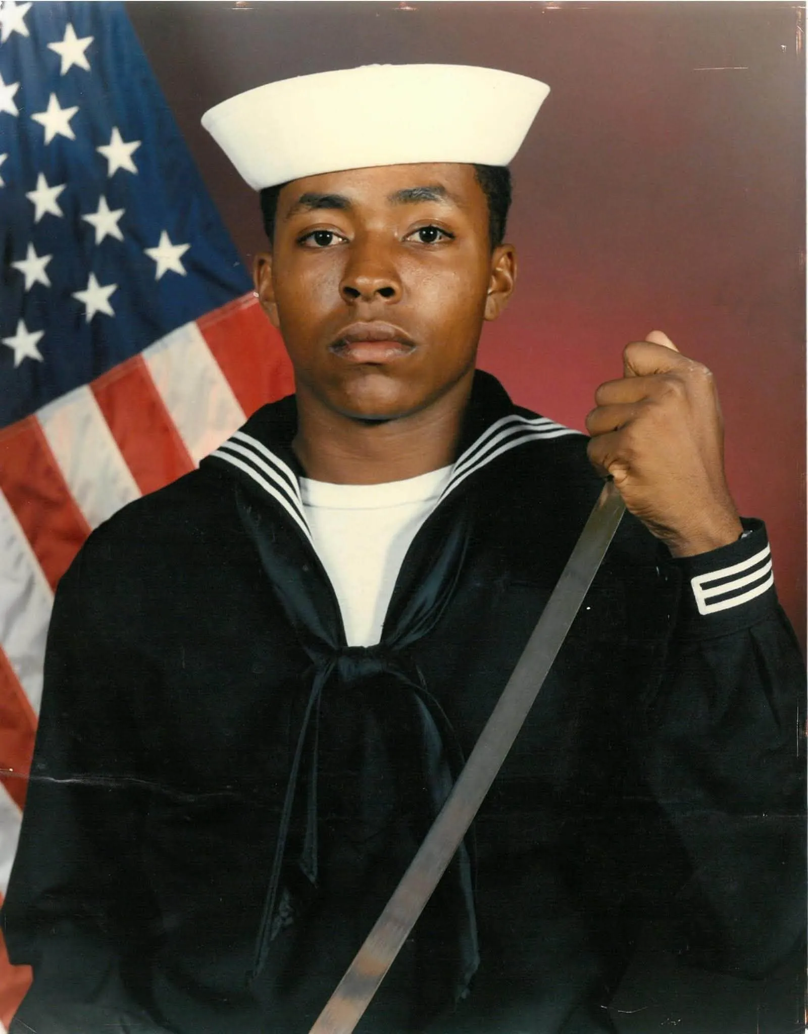 Kaleem Caire in his U.S. Navy dress uniform in front of an American flag